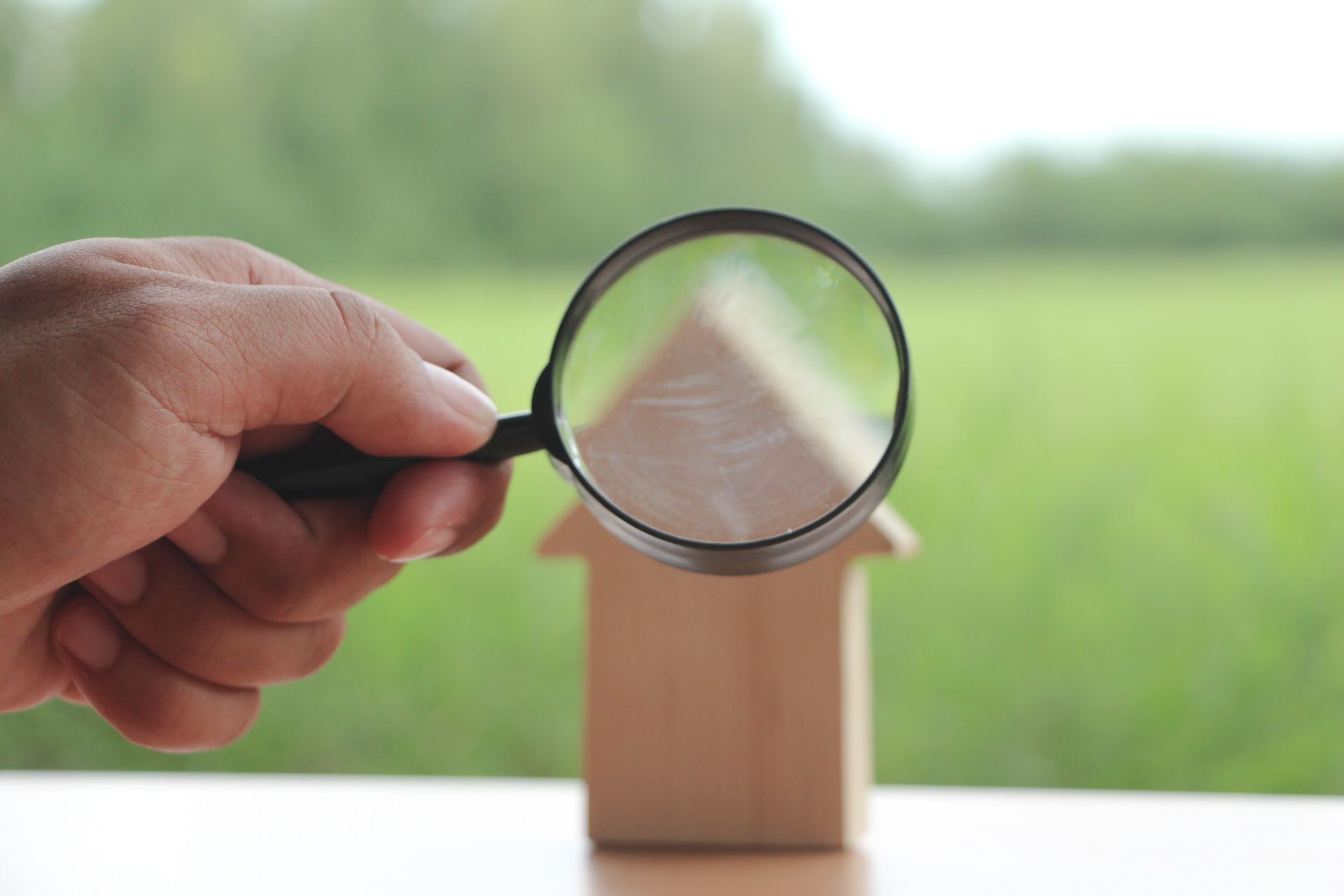 Magnifying glass with mini wood house model on green background, Home inspection concept or research estate.